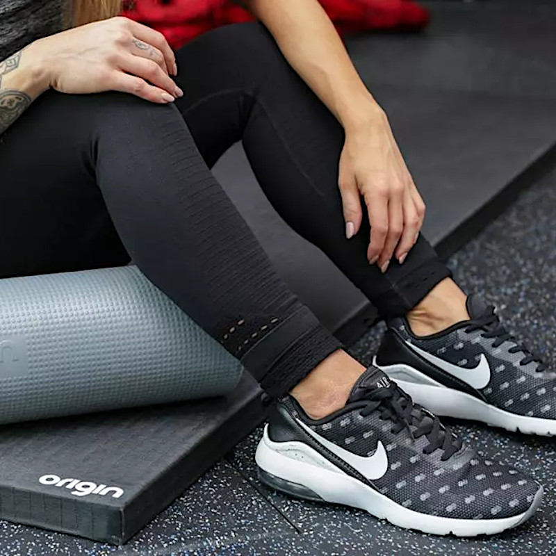 a women with black trainers sitting on an origin yoga mat with foam roller